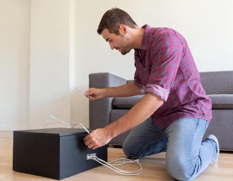 Netzwerk Einrichtung Mann kniet vor einem schwarzen Boxmöbel und verbindet Kabel.